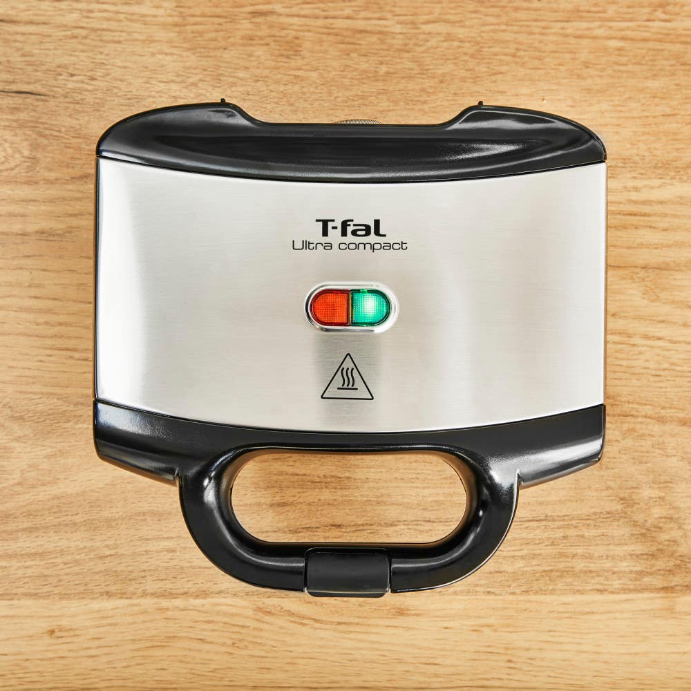 Closed sandwich maker with LED indicators on a wooden surface.