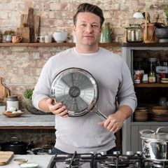 Chef standing in rustic kitchen holding stainless steel frypan with induction base