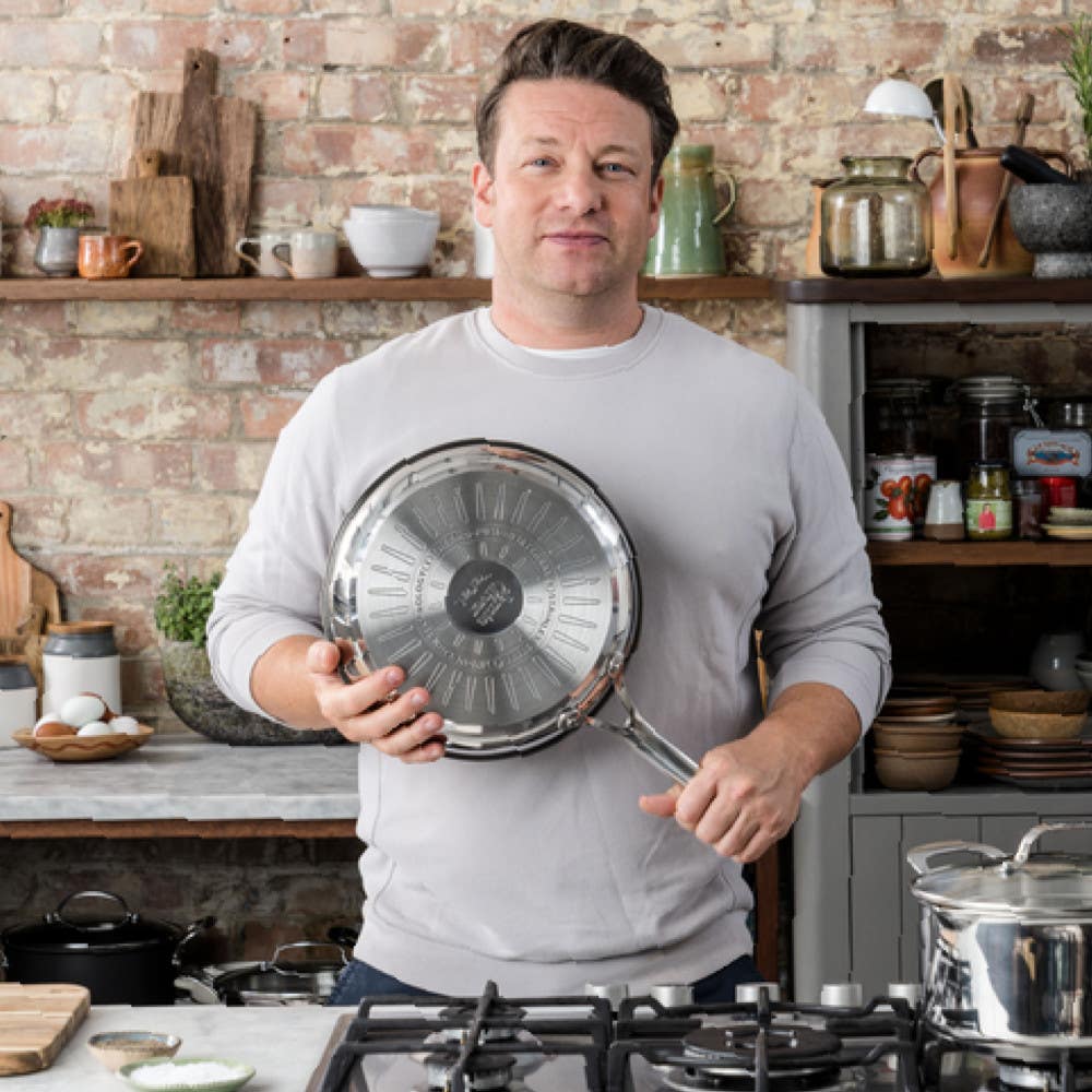 Chef standing in rustic kitchen holding stainless steel frypan with induction base