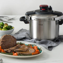 A T-fal pressure cooker on a kitchen counter with a roast beef plate, garnished with carrots and surrounded by side dishes.
