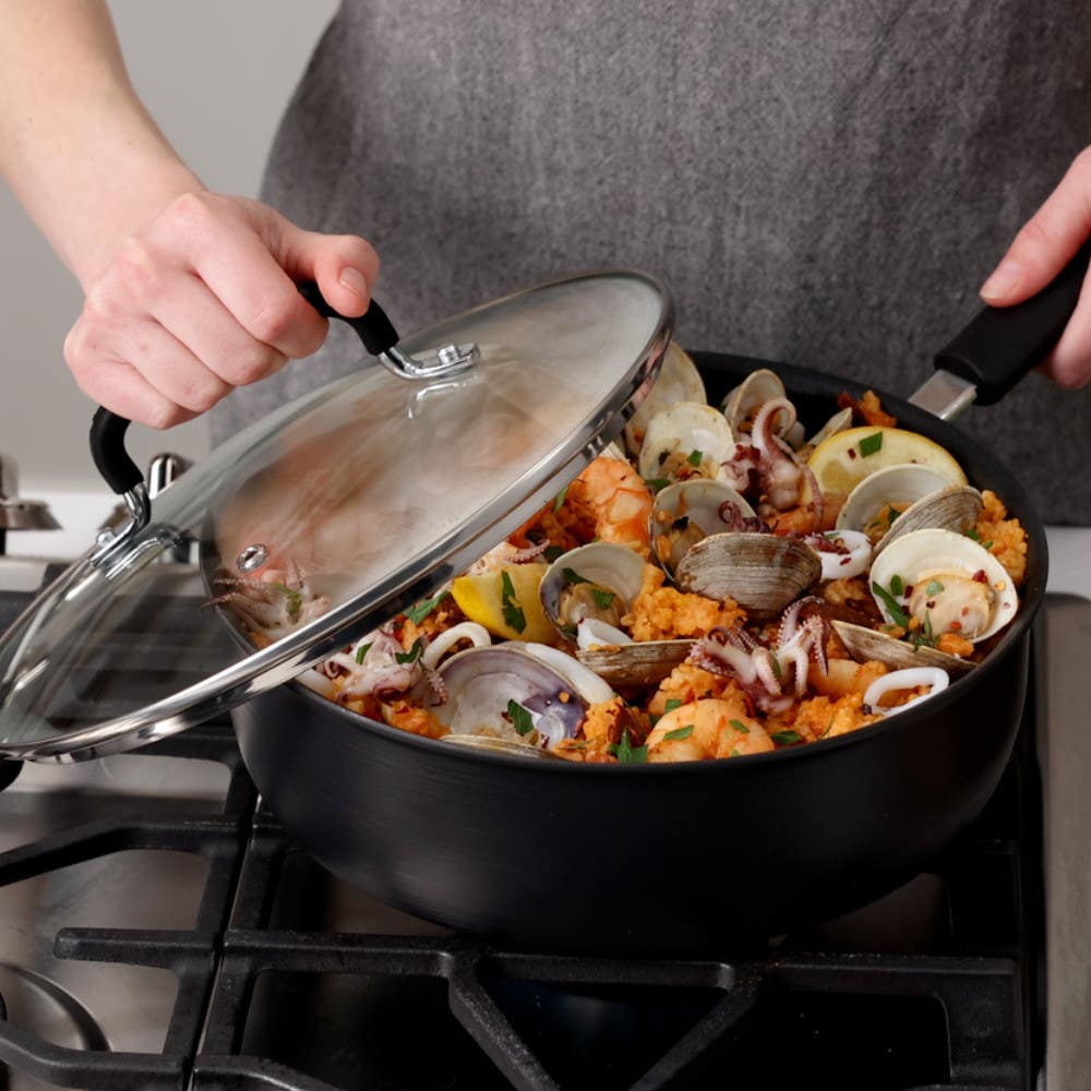 Person lifting lid off a jumbo cooker filled with seafood stewing on a stove.