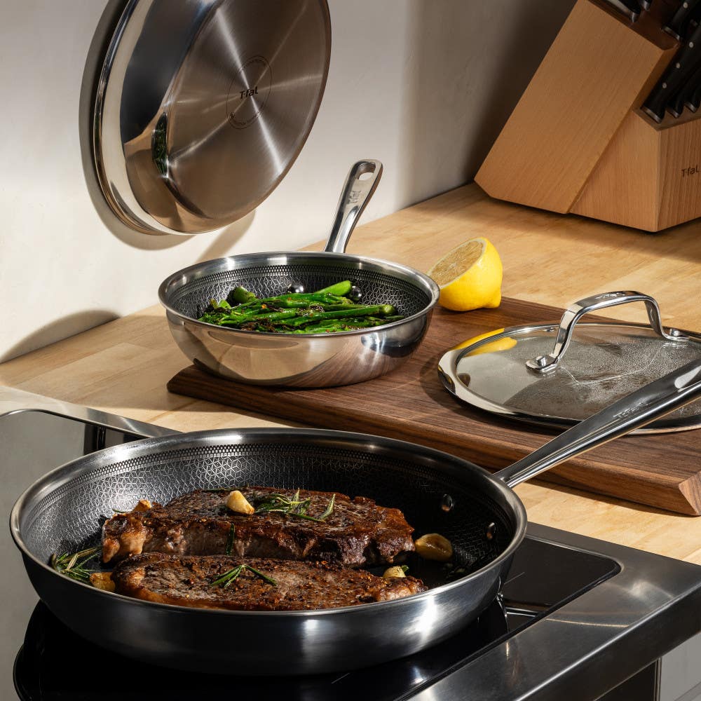 Two frying pans on an induction cooktop, one with steak and the other with asparagus