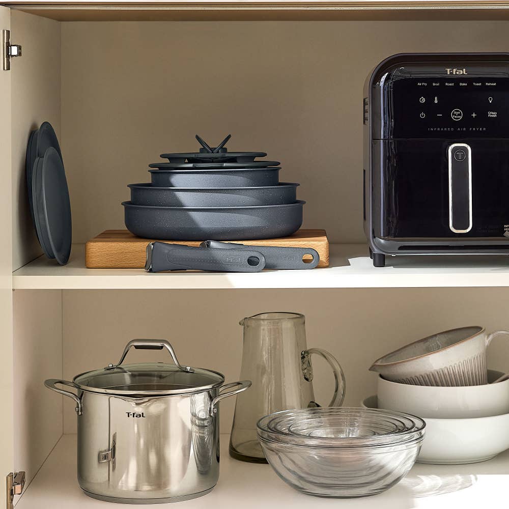 Stacked grey cookware on wood, stainless steel pot, glass bowls, plates, and an air fryer