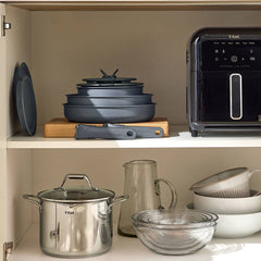 Stacked grey cookware on wood, stainless steel pot, glass bowls, plates, and an air fryer