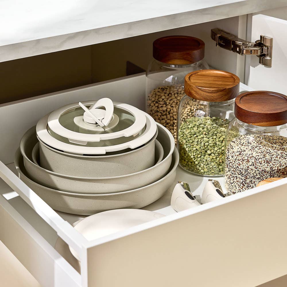 Stacked beige cookware in drawer surrounded by jars of grains showcasing organized storage