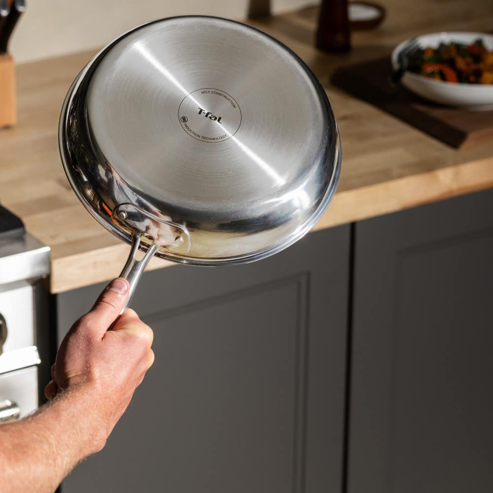 A hand holding a stainless steel frying pan showing the induction base