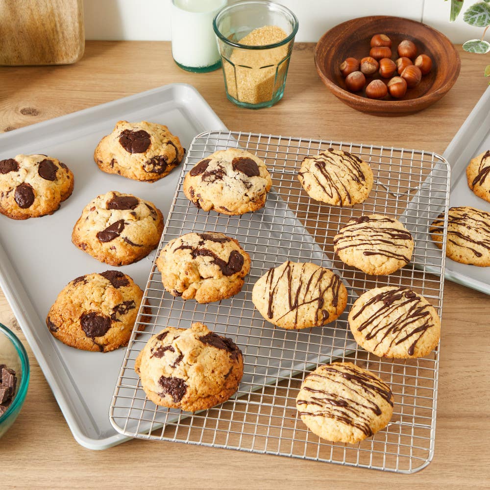 Freshly baked cookies cooling on racks; baking sheets and ingredients around.