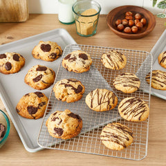 Freshly baked cookies cooling on racks; baking sheets and ingredients around.