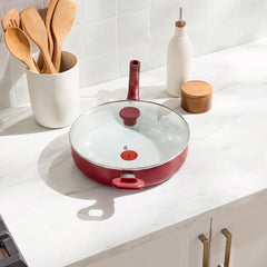 Red deep sauté pan with glass lid displayed on white countertop in kitchen