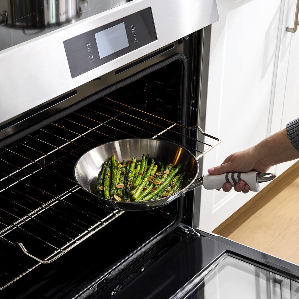 Hand placing a pan of cooked asparagus into an oven.