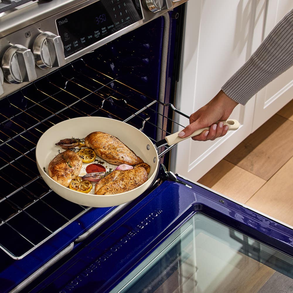 Hand placing beige nonstick frypan with chicken into oven using silicone handle