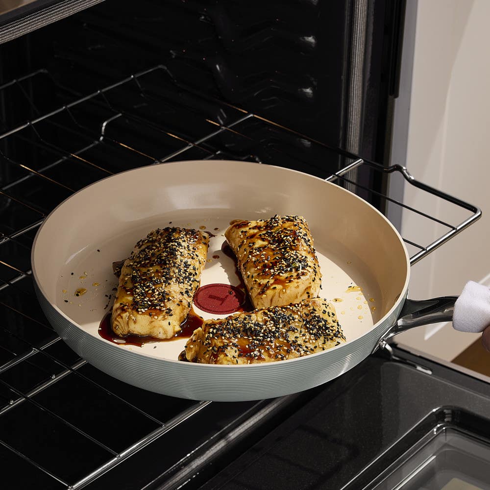 Three pieces of seasoned fish in a ceramic skillet inside an oven.