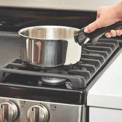 A stainless steel pot is being placed on a gas stove by a person holding its handle