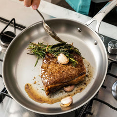 Close-up of steak searing with garlic and rosemary in stainless frypan on gas stove