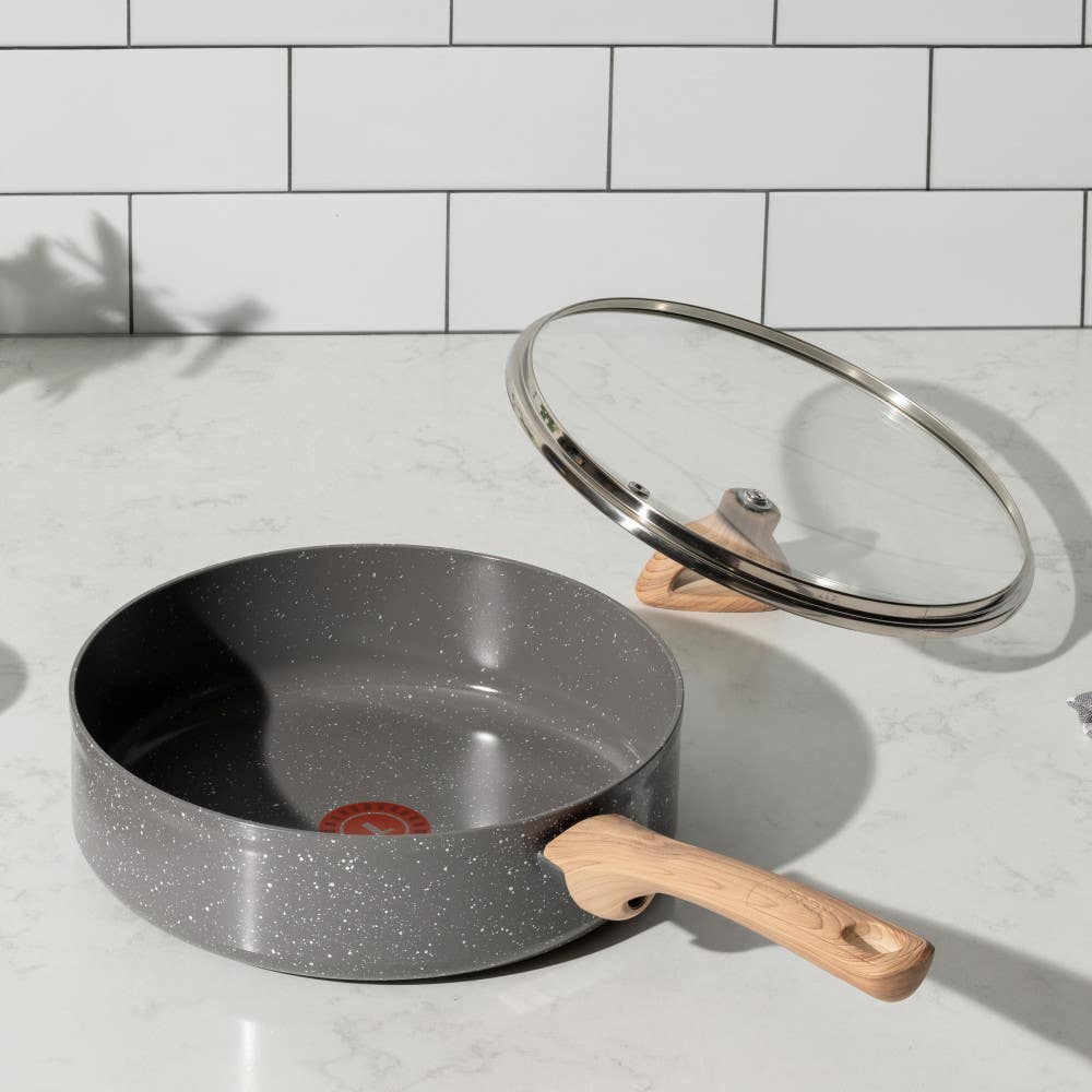 A gray frying pan with ceramic interior and wooden handle, with a lid on marble countertop