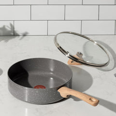 A gray frying pan with ceramic interior and wooden handle, with a lid on marble countertop