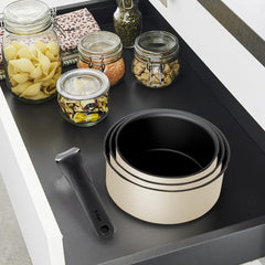 Stacked beige pots with a detachable handle in a drawer next to jars filled with dry food