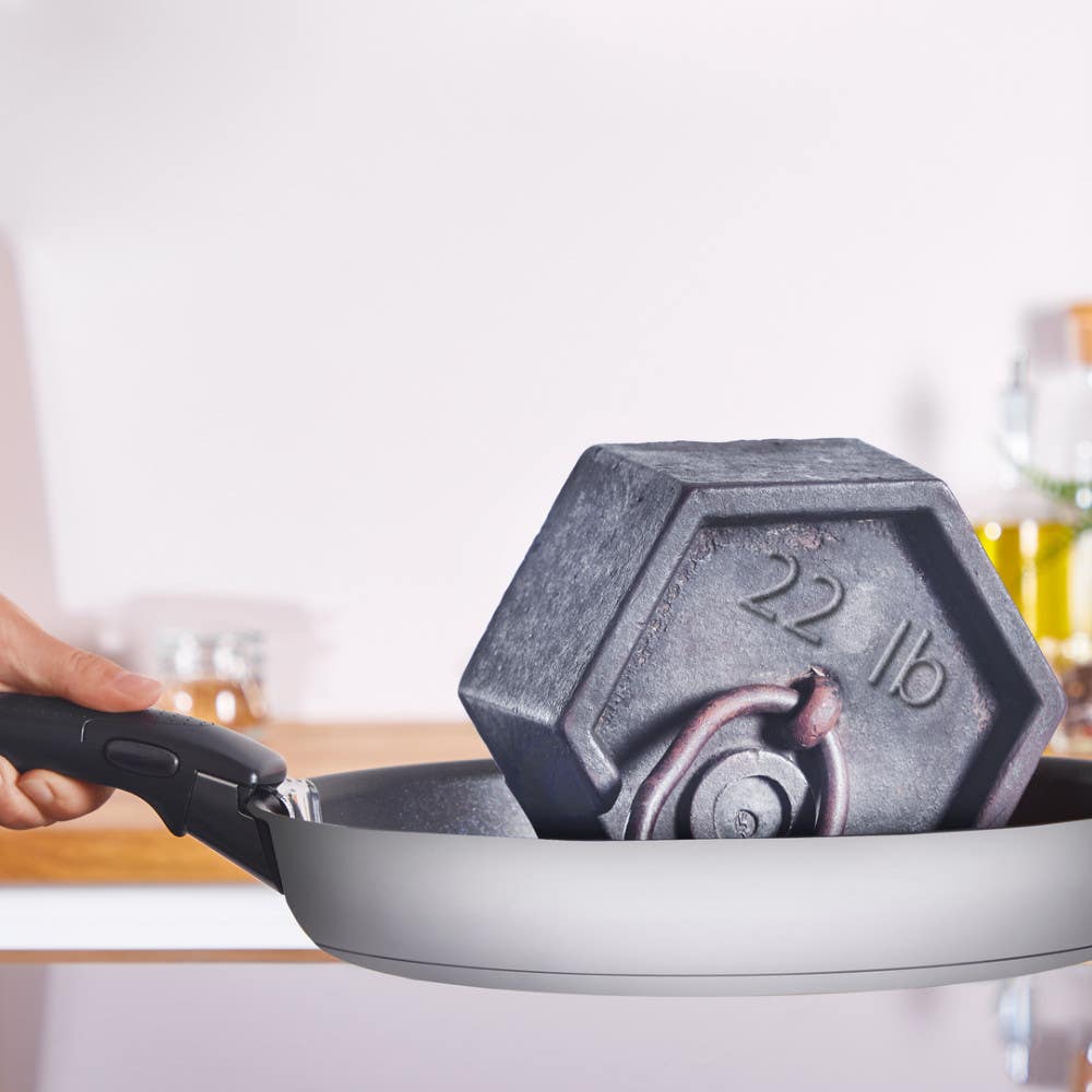 Hand holding a stainless steel frying pan with a 22 lb hexagonal weight inside