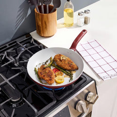 Red frypan cooking two seasoned chicken breasts with vegetables on gas stove