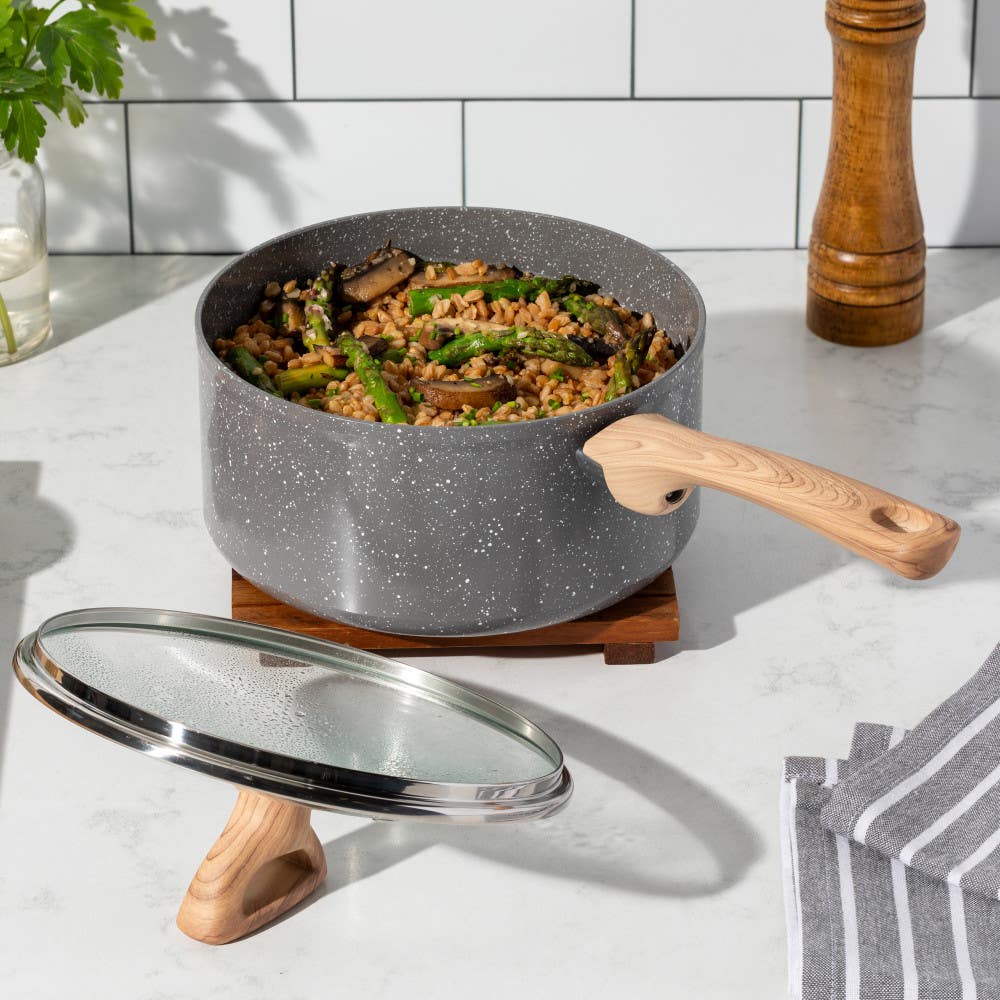 Grey ceramic saucepan with wooden handle, lid on stand, filled with lentils and vegetables