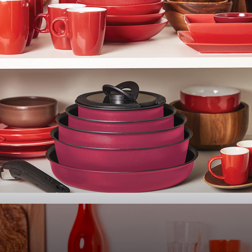 Stacked pink cookware among red and white dishware in a cabinet and a detachable handle
