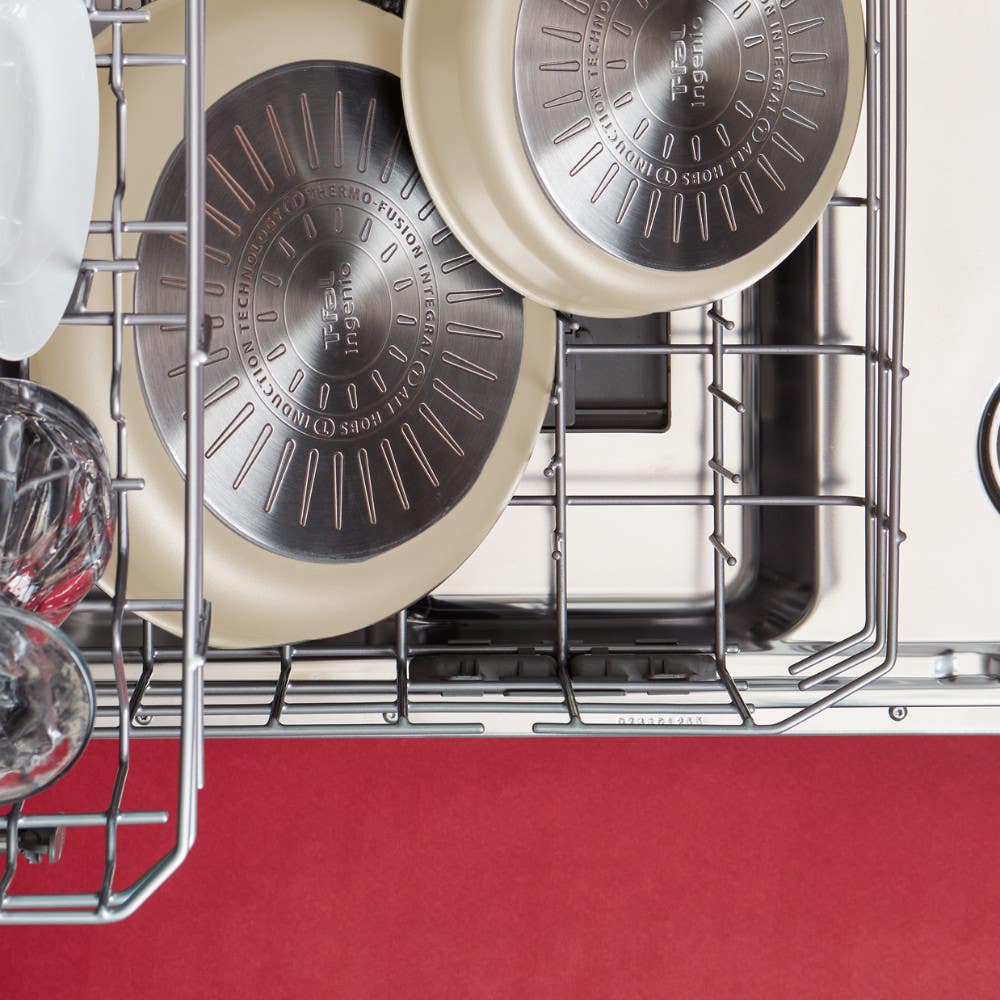 Two beige frying pans placed upside down in a dishwasher along with glass cups and plates