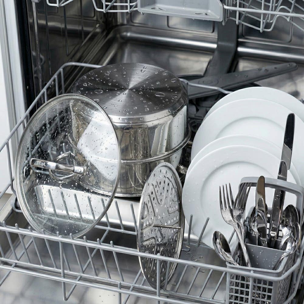 Open dishwasher with stainless steel cookware, plates, and utensils inside|