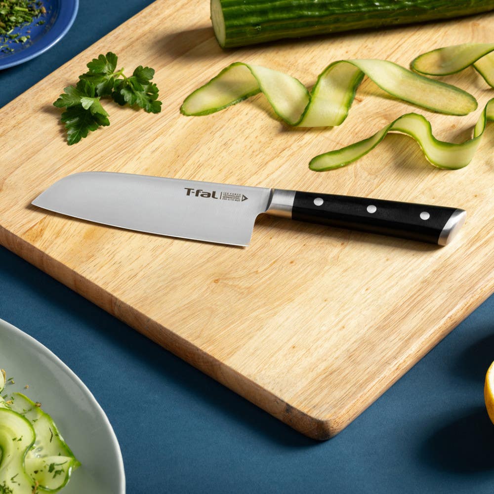 A T-fal santoku knife on a wooden cutting board with cucumber slices and parsley.