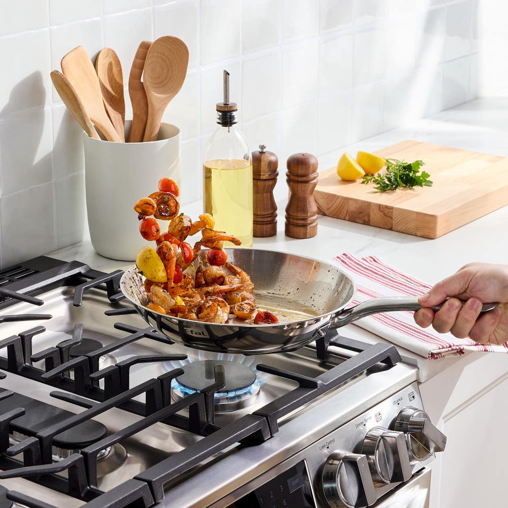 Shrimp and vegetables being sautéed in a skillet on a gas stove.