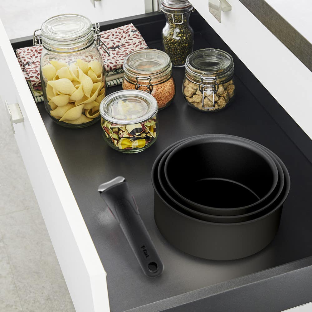 Stacked black pots with a detachable handle in a drawer next to jars filled with dry food