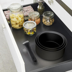 Stacked black pots with a detachable handle in a drawer next to jars filled with dry food