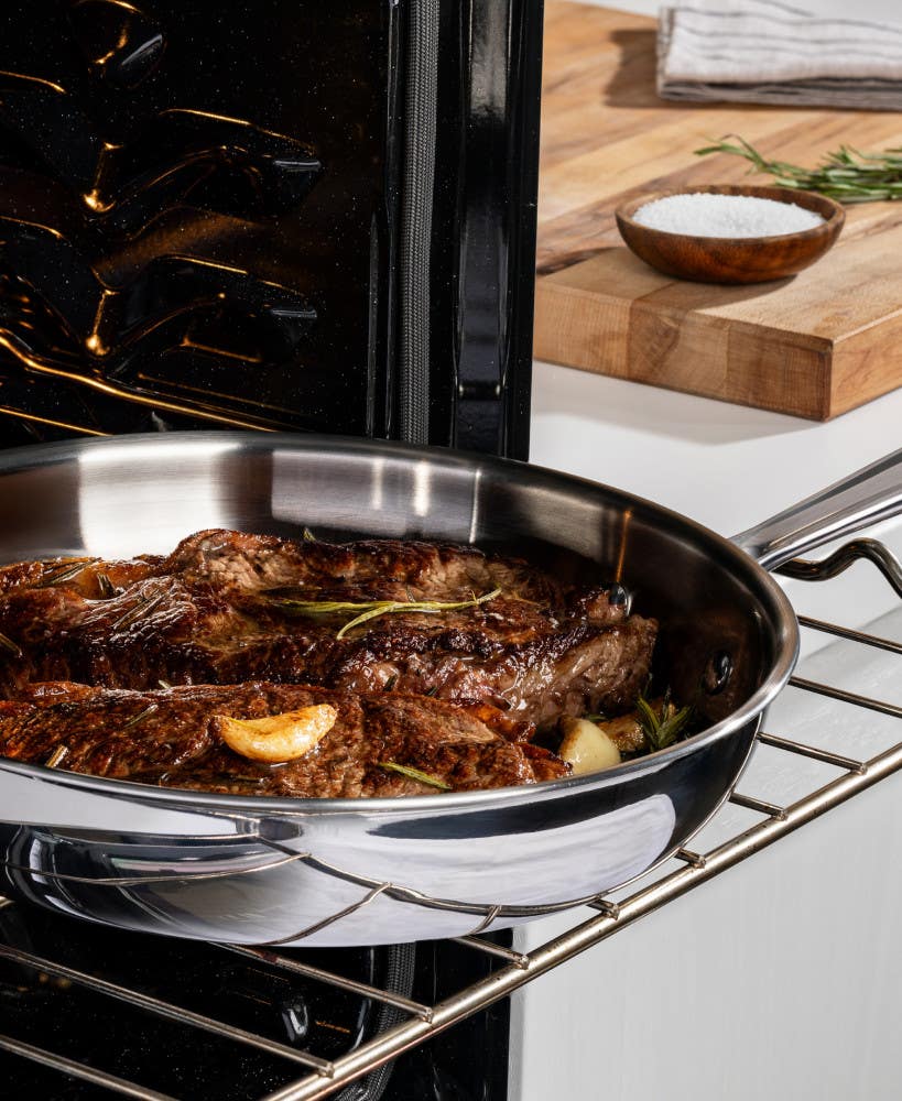 A stainless steel pan with seasoned steaks cooking in the oven on a rack