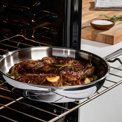 A stainless steel pan with seasoned steaks cooking in the oven on a rack