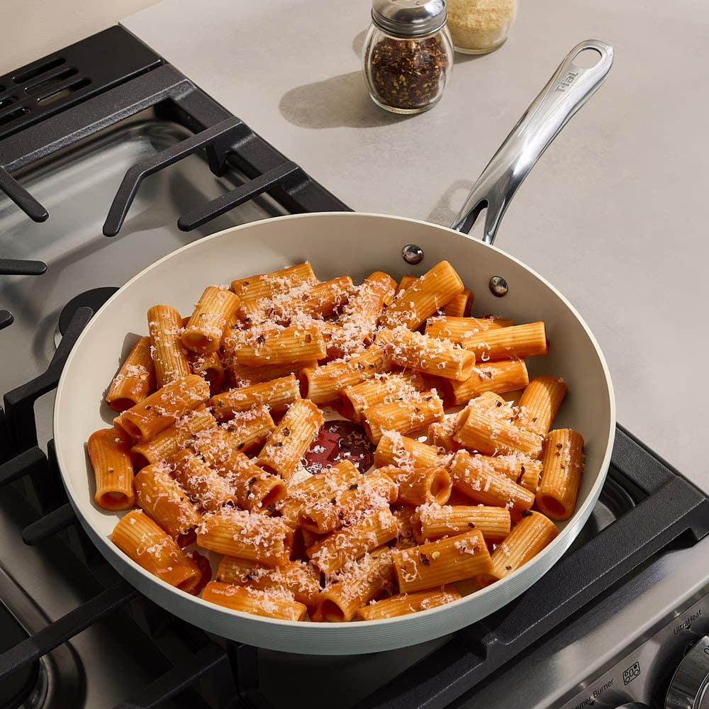 Rigatoni pasta with tomato sauce and grated cheese in a ceramic skillet on a gas stove.