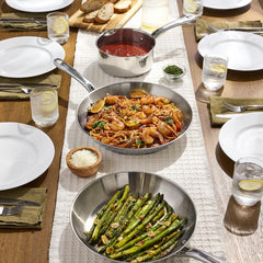 Table set for a meal with pasta, asparagus, sauce, bread, and glasses of water with lemon.