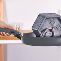 A grey frying pan holding a grey 22 lb weight, with a hand grasping the handle