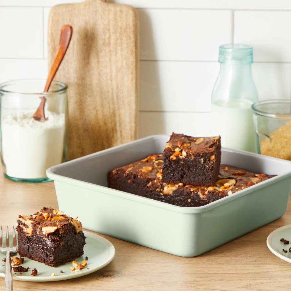Brownies in a green square dish surrounded by baking ingredients.