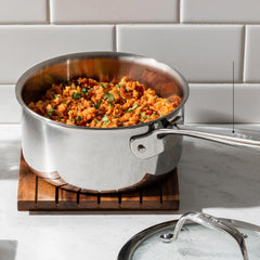 Stainless steel saucepan on a trivet, filled with a cooked dish garnished with green herbs