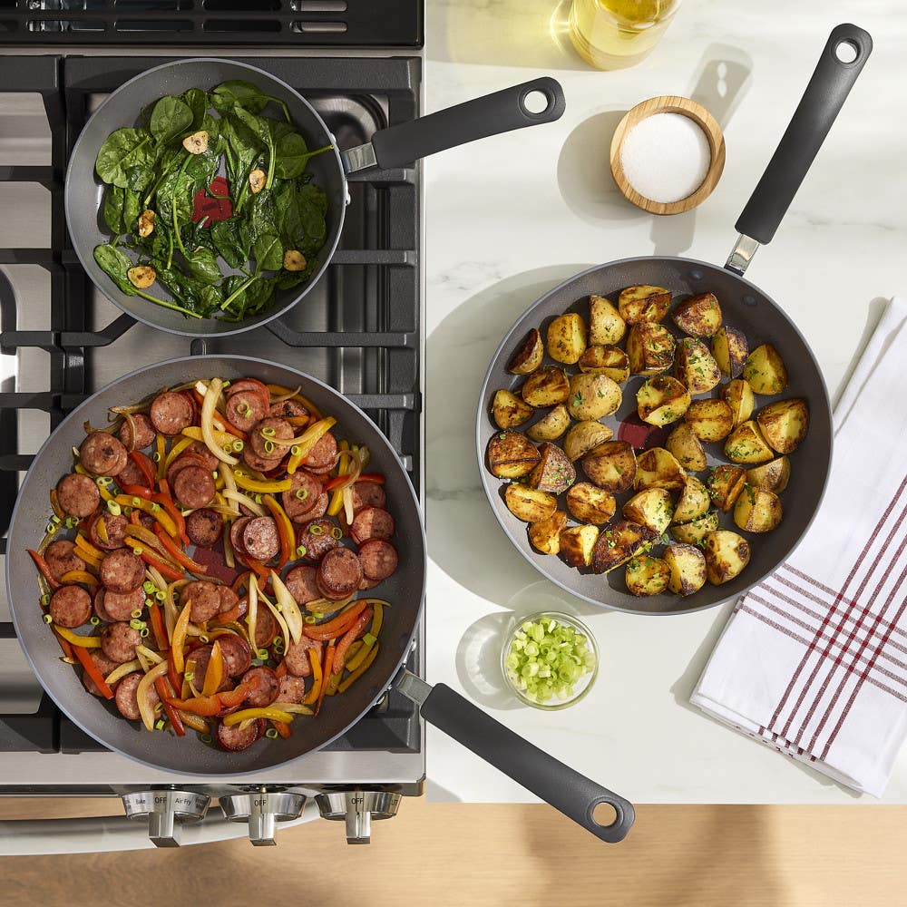 Overhead view of three pans with sautéed spinach, roasted potatoes, and sausage with peppers.