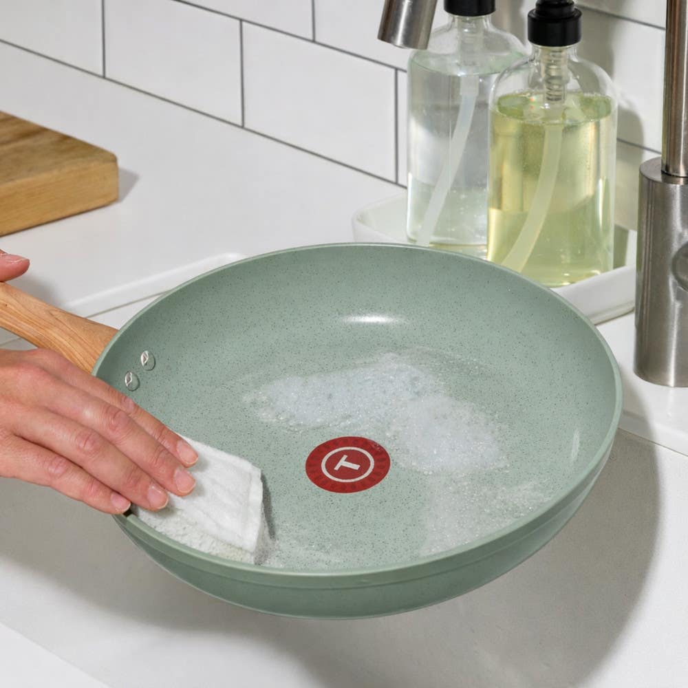 T-fal green ceramic frypan washed with a sponge under running kitchen faucet