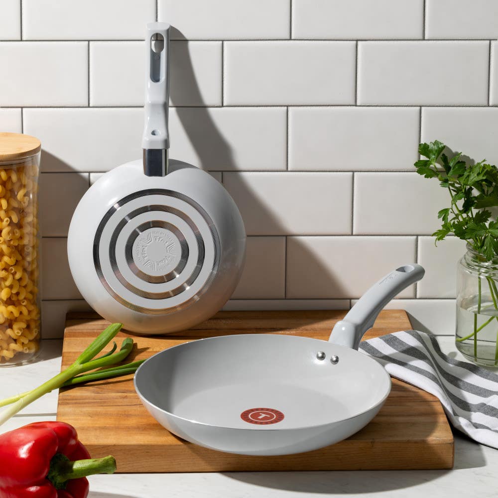 Two grey ceramic frypans: one standing showing the base, the other over a wooden board