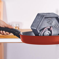 A red frying pan holding a grey 22 lb weight, with a hand grasping the handle
