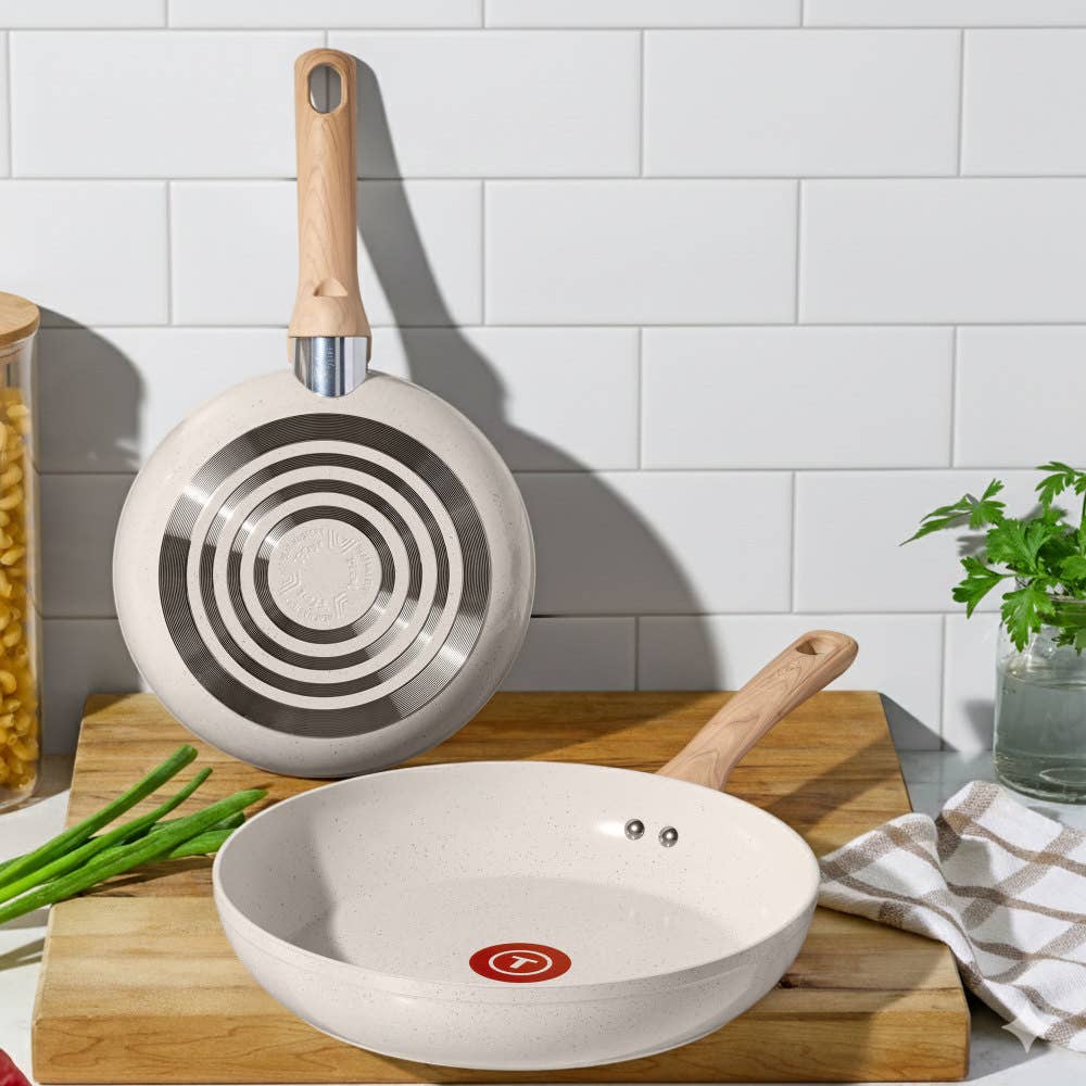 Two beige T-fal ceramic frypans, one over a wood cutting board, one showing base against wall