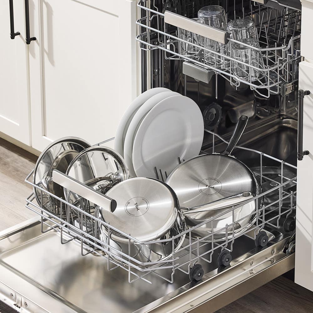Image of stainless steel cookware, glass lids, and plates loaded in a dishwasher bottom rack, glasses on the top rack.